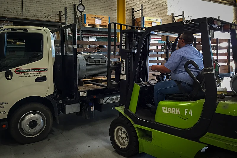 Electric Motor Shop technician unloading industrial motor from delivery truck with forklift for repair documentation and inspection.