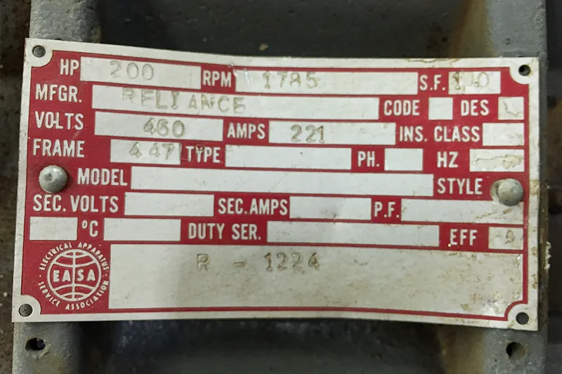 Close-up of Reliance motor nameplate showing electrical specifications for documentation during repair process at Electric Motor Shop.