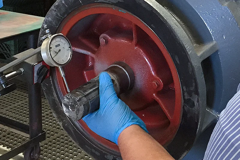 Technician using dial indicator to check motor shaft trueness before disassembly.