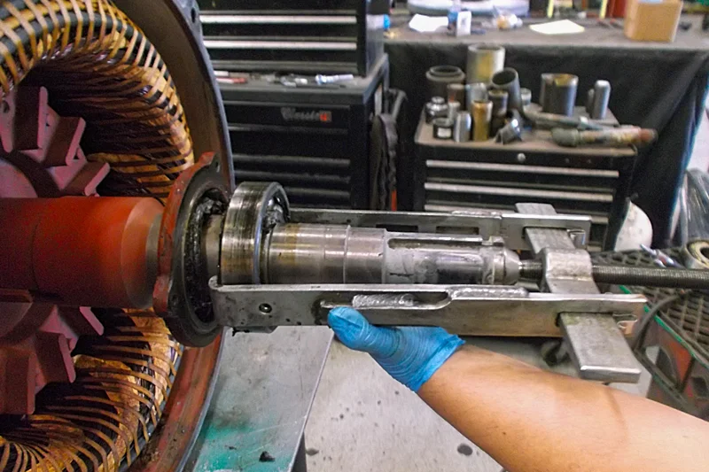 Technician removing motor bearing during disassembly to inspect shaft and internal wear.