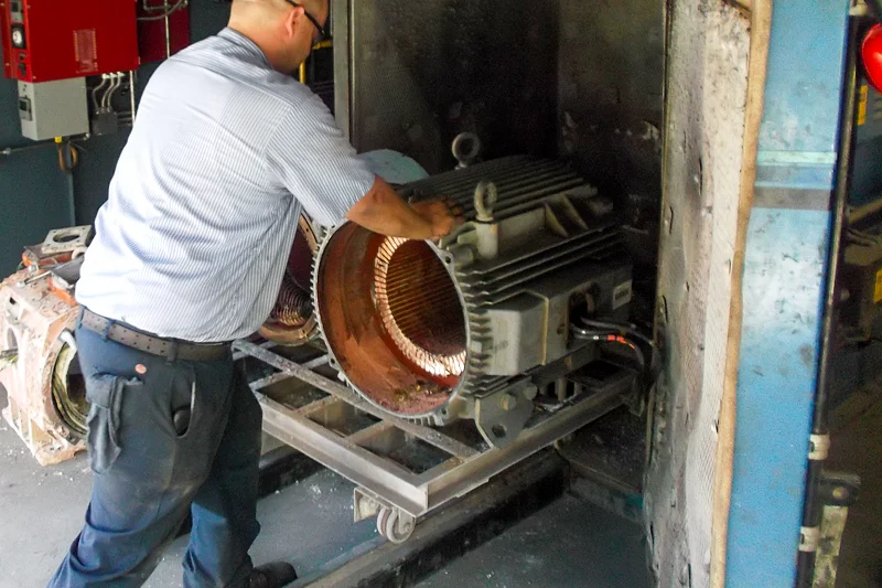 Technician at Electric Motor Shop loading stator into flame-controlled burnout oven for insulation removal without damaging core.