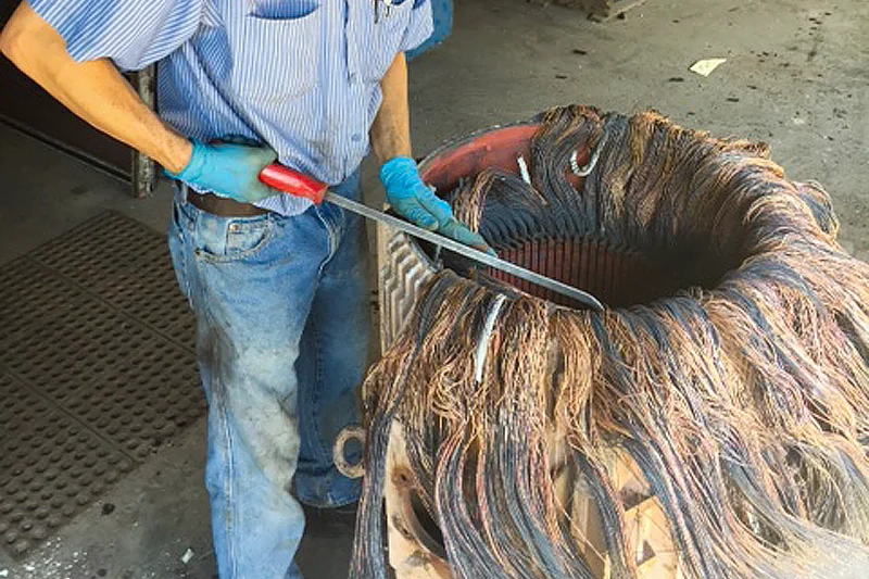 Technician manually extracting burnt stator windings with hand tools to prepare for documentation and rewind.