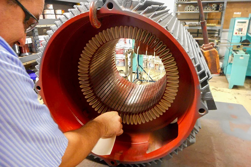 Electric Motor Shop technician placing NOMEX insulation paper into stator slots in preparation for new winding coils.