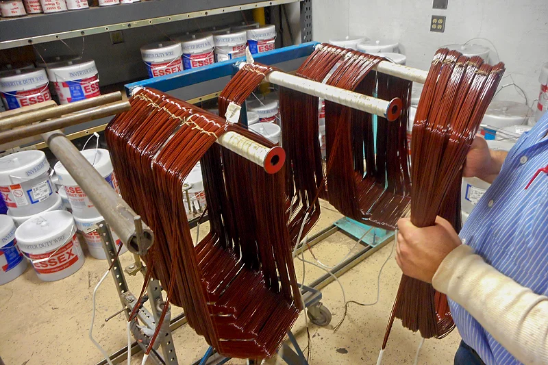 Technician organizing freshly wound and labeled motor coils for installation during stator rewind process.