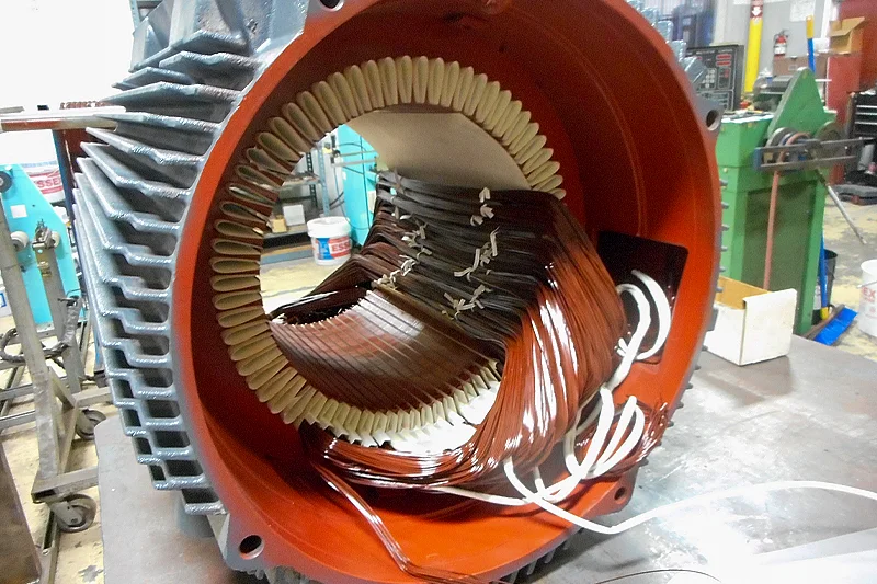 Newly wound motor coils hand-inserted into stator slots with phase insulation for electrical separation and protection.
