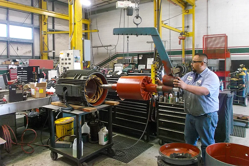 Technician using a hoist to carefully align and install the rotor into the stator housing on a workbench.