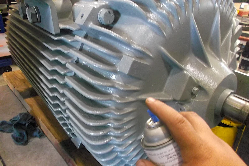 Technician applying touch-up spray paint to the motor’s exterior housing during the final reassembly phase.
